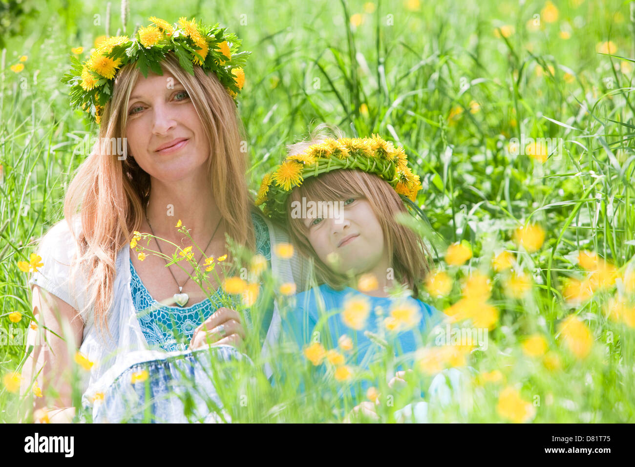 Mère et fils avec des couronnes de fleurs assis dans une prairie au printemps Banque D'Images