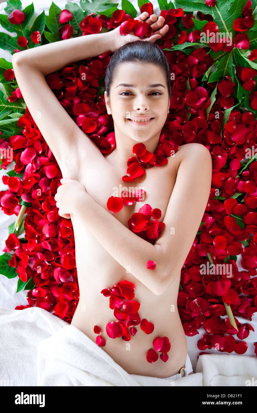 Jeune femme allongée sur le dos contre des pétales de rose. Banque D'Images