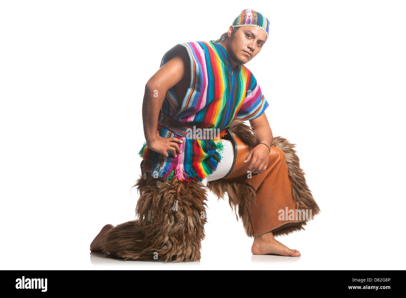 Un homme pose dans une position dynamique accroupie sur un fond blanc Uni. Il porte une tunique sans manches rayée multicolore vibrante avec ourlet frangé, un bandeau à motifs assorti et marron Banque D'Images