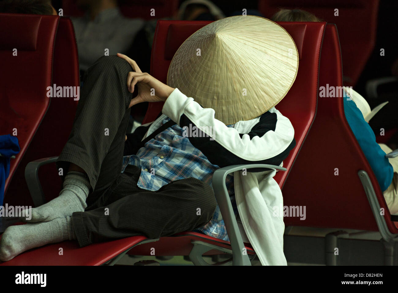 Homme portant un chapeau de bambou asiatique pendant le sommeil, Dubai International Airport Terminal Banque D'Images