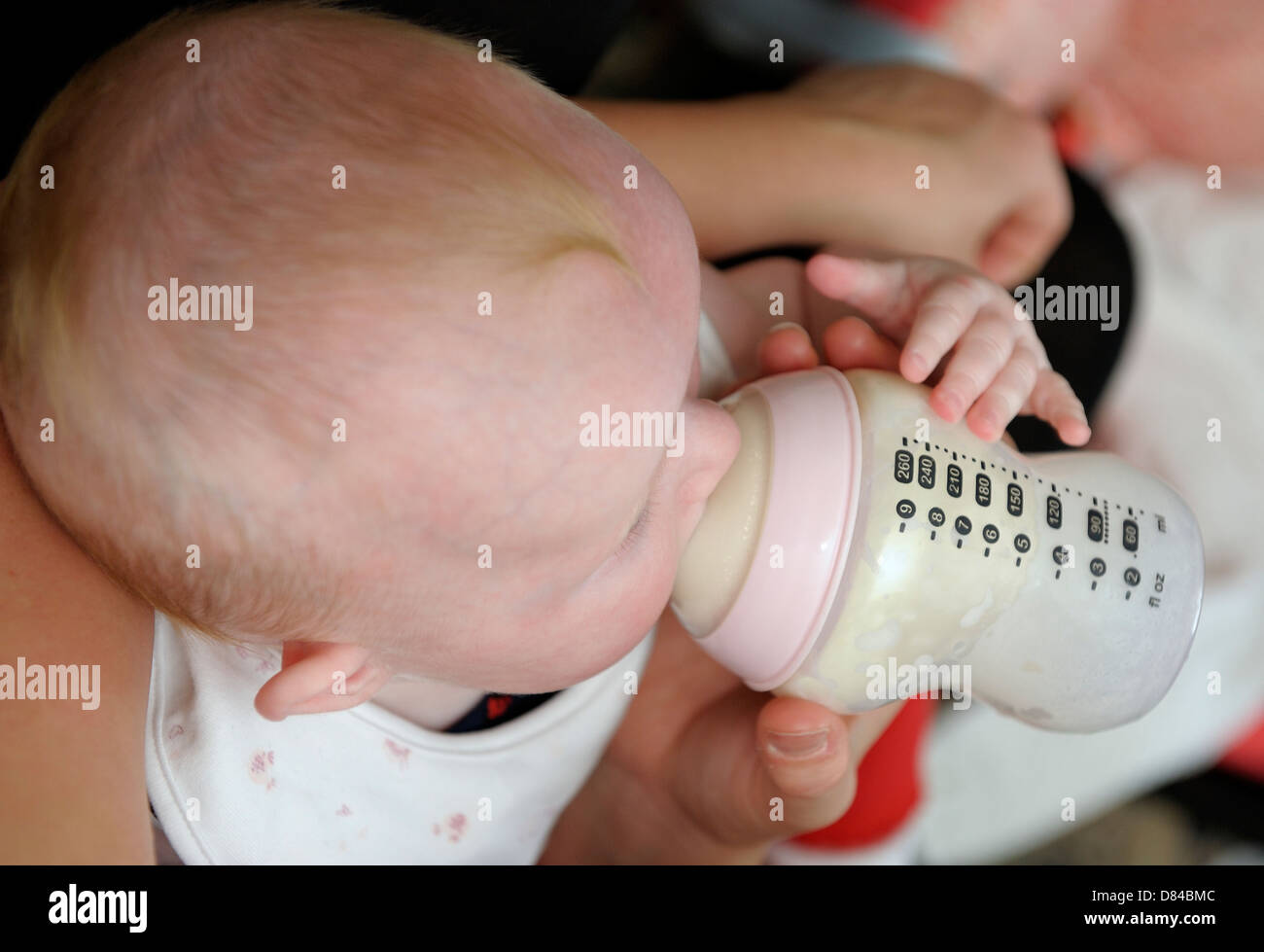 Baby Girl holding bouteille tout en étant nourri Banque D'Images