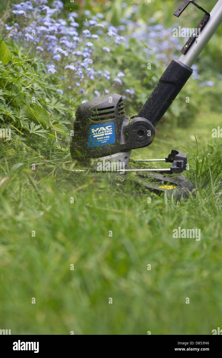 Strimming la longue herbe contre une fleur frontière dans un jardin anglais Banque D'Images