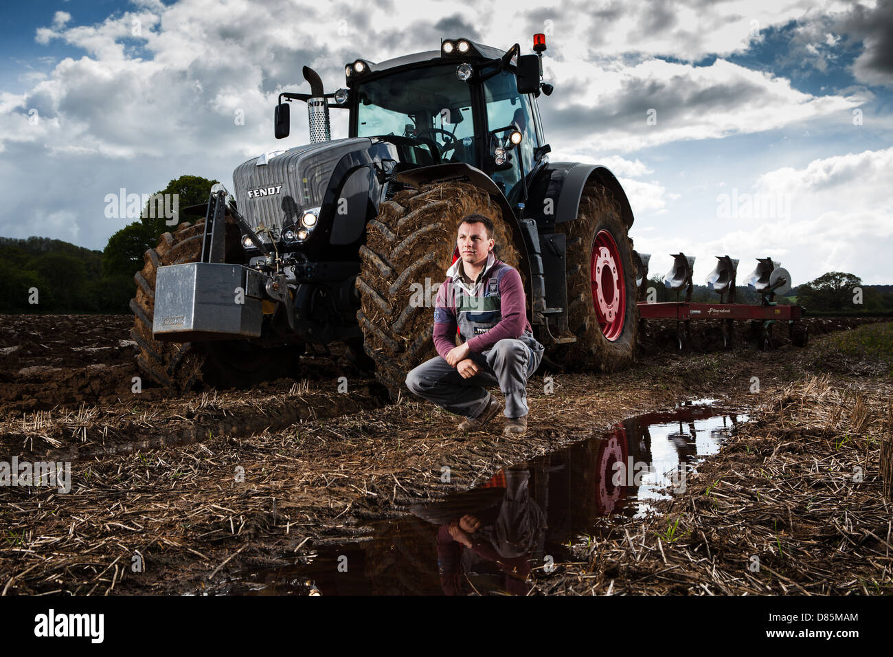 Portrait d'un jeune agriculteur avec tracteur et charrue dans le champ labouré. Banque D'Images