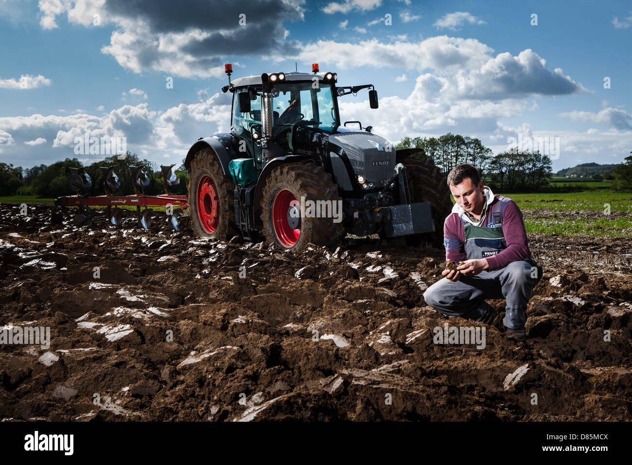 Portrait d'un jeune agriculteur avec tracteur et charrue dans le champ labouré. Banque D'Images