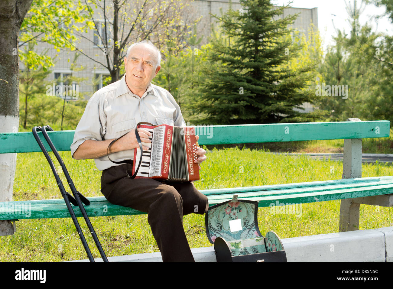 Mobilité senior avec une jambe amputée au-dessus du genou assis sur un banc de parc à jouer de l'accordéon Banque D'Images