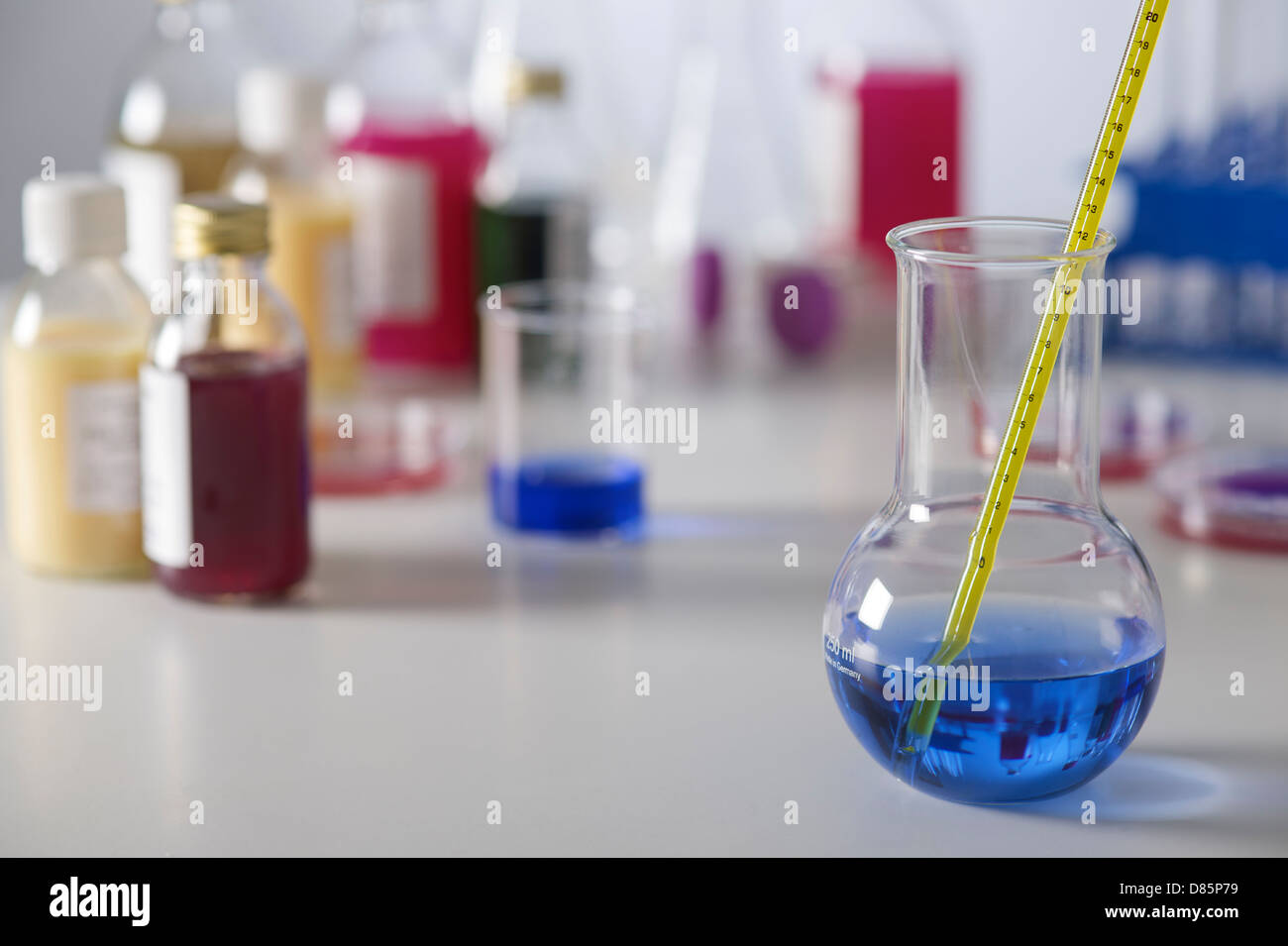 Matériel de laboratoire de sciences avec l'ampoule de verre tube à essai dans l'avant-plan bleu contenant des produits chimiques et thermomètre sur Workbench. Banque D'Images