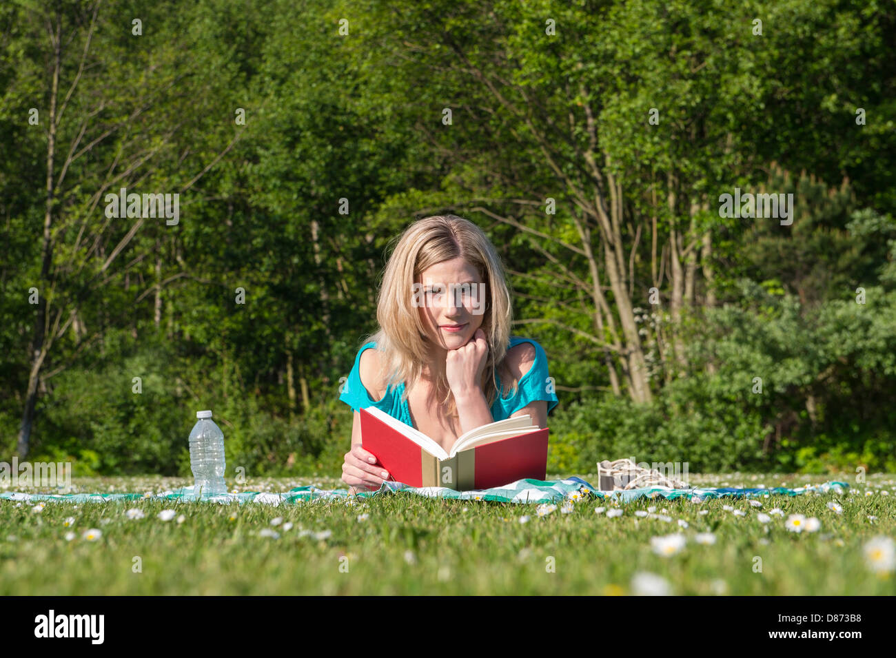 Portrait of beautiful young woman reading book while lying on grass at park Banque D'Images