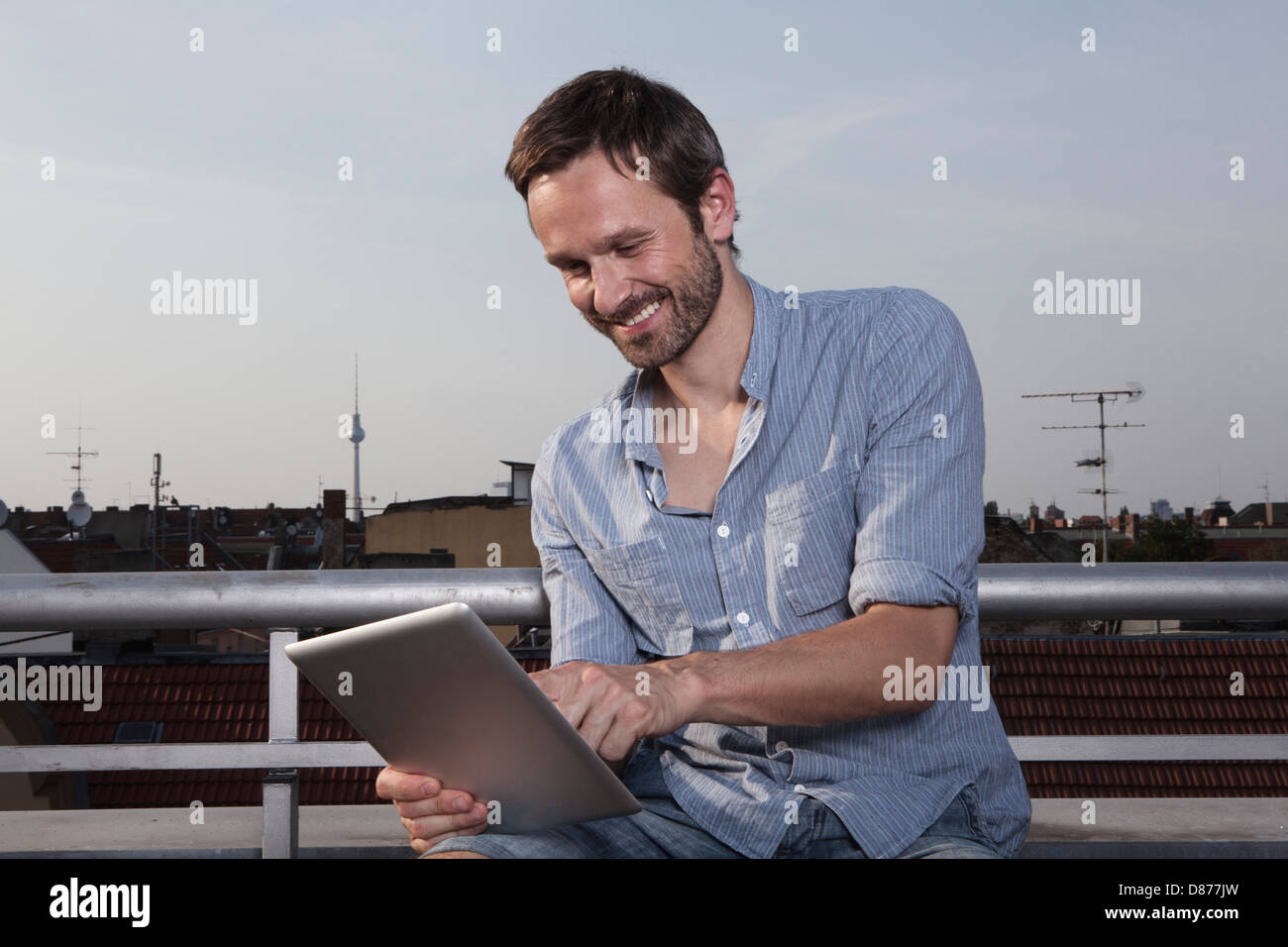 Allemagne, Berlin, Man using digital tablet sur la terrasse du toit, smiling Banque D'Images