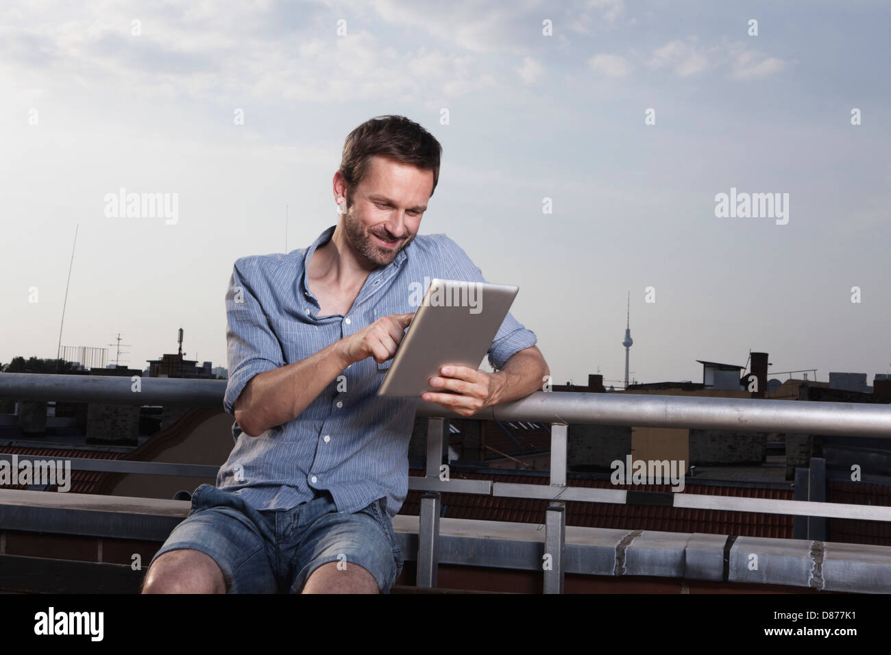 Allemagne, Berlin, Man using digital tablet sur la terrasse du toit, smiling Banque D'Images