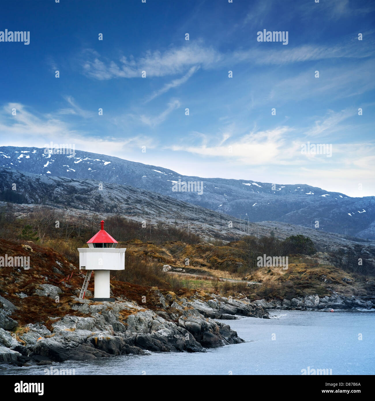 Phare norvégien. Tour blanche avec haut rouge se dresse sur les rochers côtiers sous ciel bleu Banque D'Images