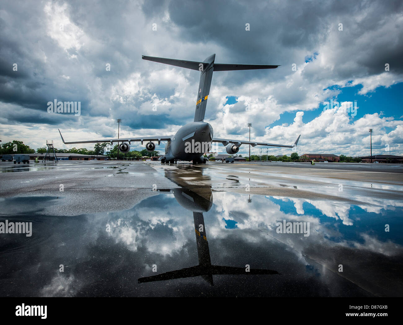 Le C-17 Globemaster III, un gros avion de transport militaire, se reflète dans une flaque d'eau de pluie, mettant en valeur son design élégant et sa taille impressionnante. Cet avion est crucial pour les missions de transport aérien lourd dans le monde entier. Banque D'Images
