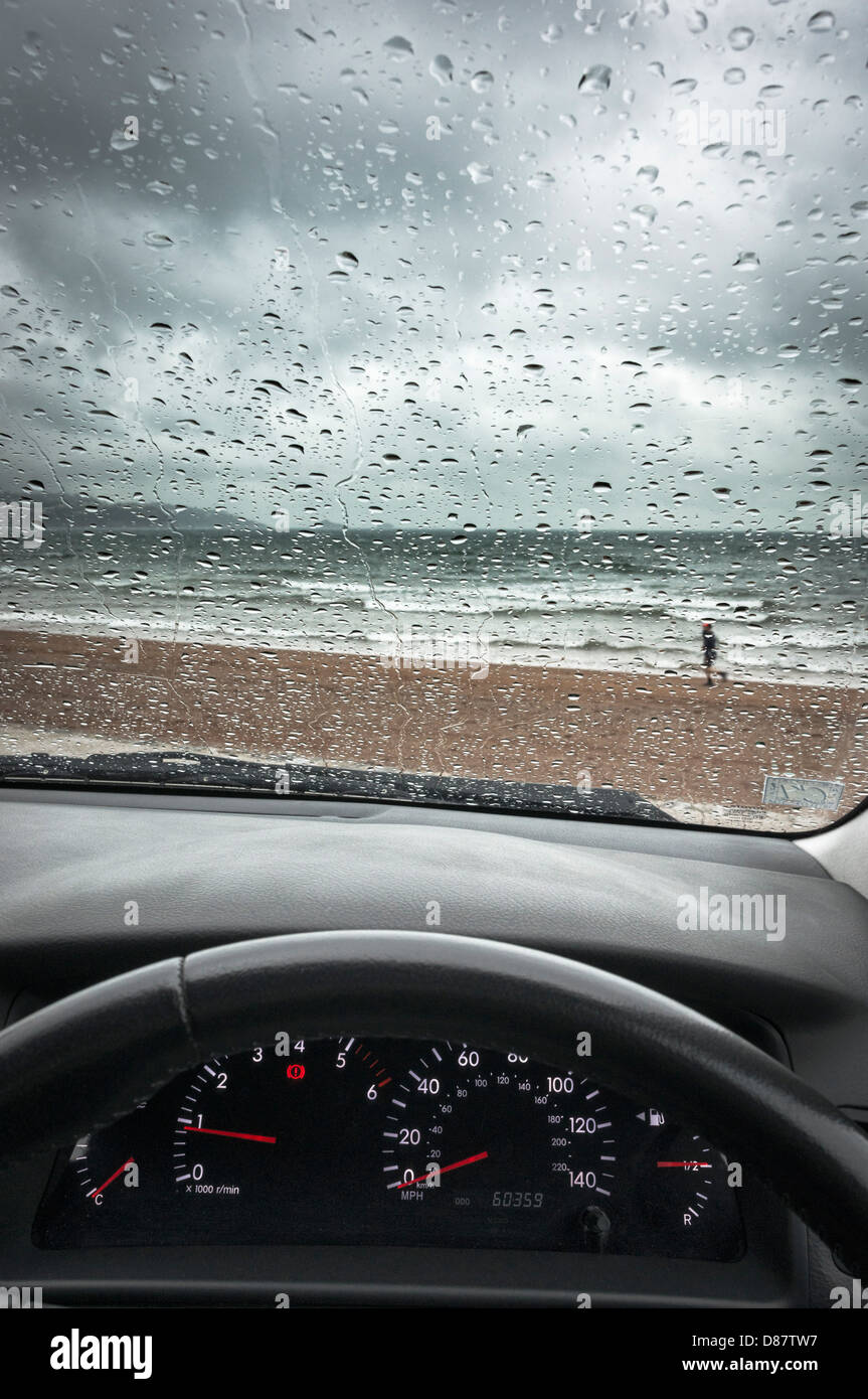 Pluie Royaume-Uni, plage de la côte sud à travers un pare-brise de voiture sur un jour de pluie au printemps / été avec un homme en cours d'exécution Banque D'Images