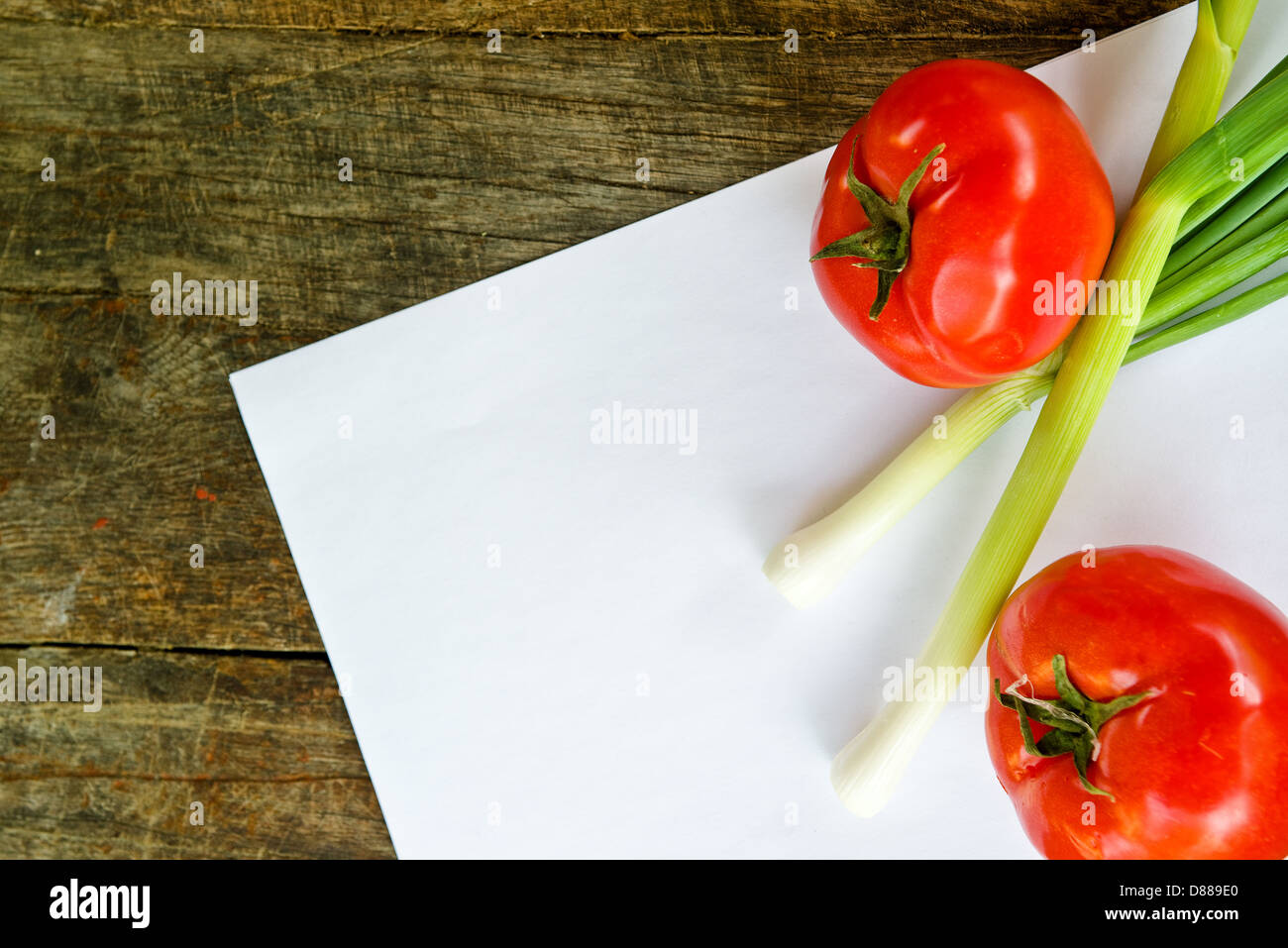 Tomate et oignon de printemps sur le papier pour la recette des notes, sur table en bois. Banque D'Images