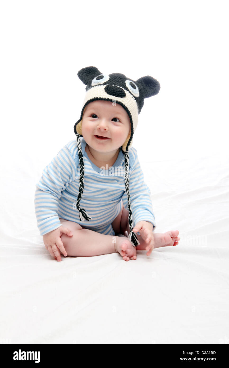 Beau rire happy baby boy sitting on bed in white hat tricoté Banque D'Images