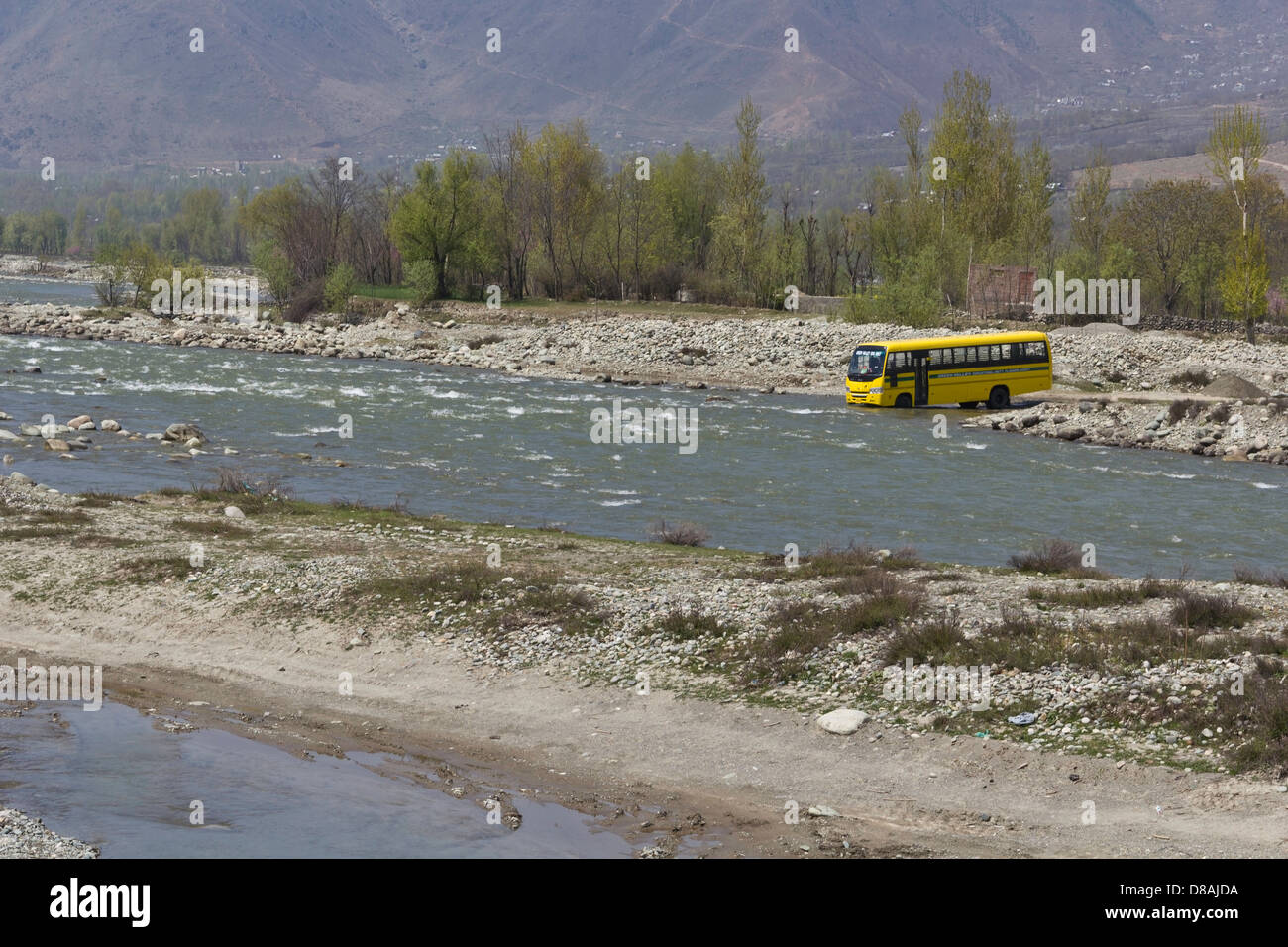 School bus dans un ruisseau de montagne dans la banlieue de Srinagar, au Cachemire, en Inde, en cours de nettoyage. L'arrière-plan sont les arbres et mur de pierre Banque D'Images