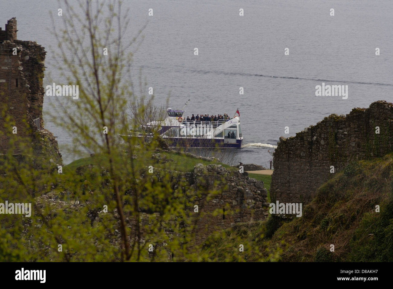 Les touristes dans un bateau de tourisme sur le Loch Ness à travers les ruines de l'Urquhart Castle. Voir à travers les murs en ruine, avec l'usine. Banque D'Images