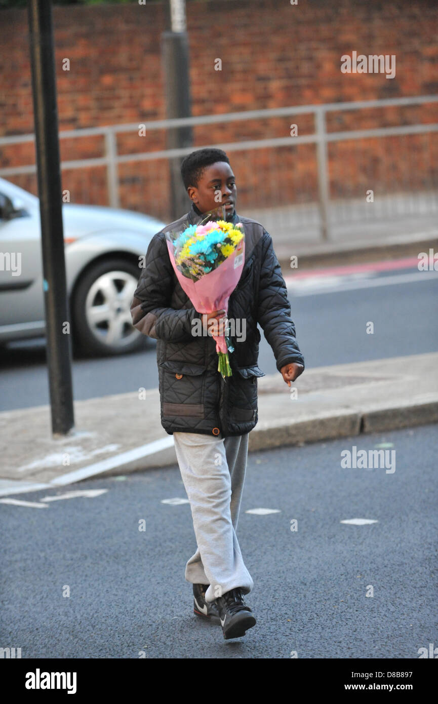 Woolwich, Londres, Royaume-Uni. 23 mai 2013. Un jeune garçon porte les fleurs à laisser sur les grilles près du lieu du meurtre. Les fleurs sont laissés par les bienfaiteurs le long des rampes près de l'endroit où le batteur Lee Rigby du 2e Bataillon du Régiment royal de fusiliers a été tué hier à l'extérieur des casernes de Woolwich. Crédit : Matthieu Chattle/Alamy Live News Banque D'Images