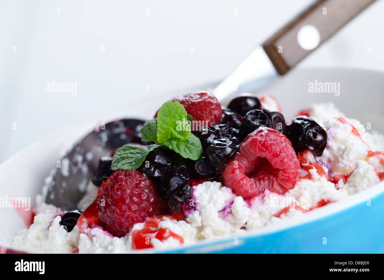 Le fromage cottage dans bol bleu avec des framboises myrtilles et menthe Banque D'Images