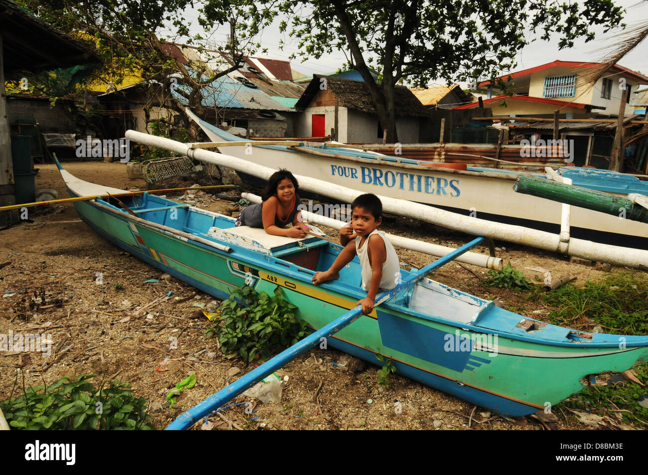 Filipino garçon et fille jouer dans un bateau de pêcheurs sur la rive à Puerto Galera. Tempête sur l'île de Mindoro, Philippines Banque D'Images