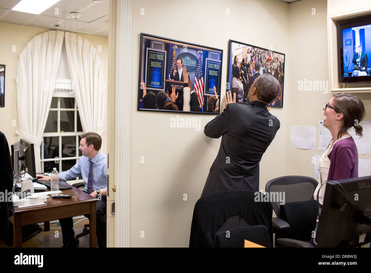 Assistant de presse Marie Aberger réagit comme le président américain Barack Obama ajuste photographies dans le bureau de presse de la Maison Blanche le 19 avril 2013 à Washington, DC. Josh Earnest, Secrétaire de presse adjoint principal, travaille dans son bureau à gauche. Banque D'Images
