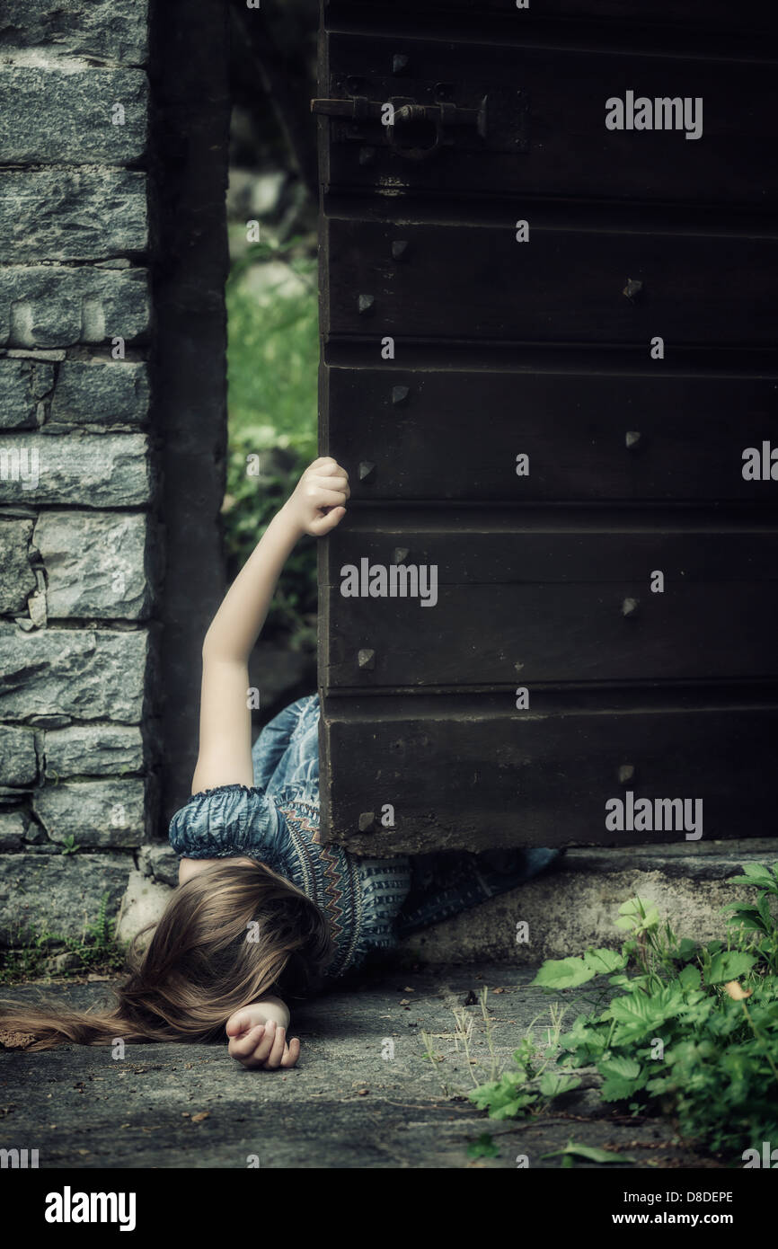 Une jeune fille allongé sur le sol près d'une vieille porte, essayant de se lever Banque D'Images
