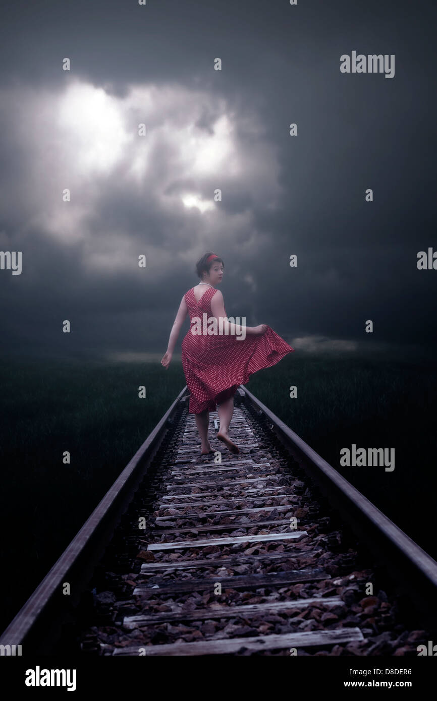 Une fille dans une robe rouge est en cours d'exécution sur des rails de chemin de fer Banque D'Images
