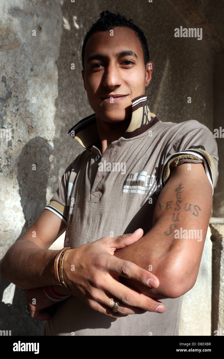 Jeune homme chrétien copte égyptien catolic montre fièrement son Jésus tatouage au bras. Village de Haute Egypte Banque D'Images