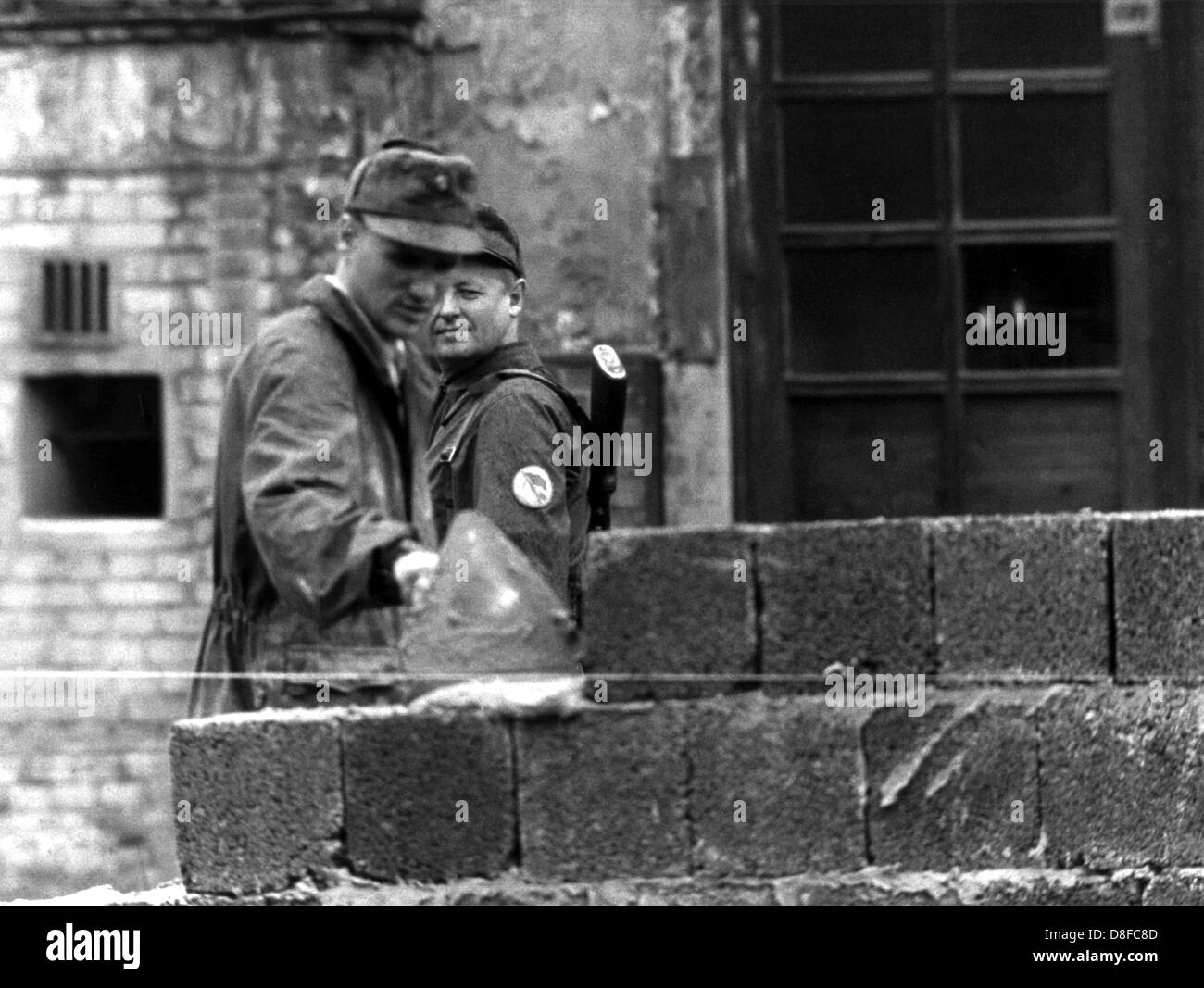 Un travailleur de la construction de Berlin est un errects-tête haut mur dans le sens de 'Lindenstrasse' street sous la supervision d'un agent de la police nationale à la Place de Potsdam à la frontière du secteur soviéto-américain de Berlin, RDA, 18 août 1961. Déjà dans la matinée du 13 août, les forces armées de la RDA avait commencé à isoler Berlin-est avec barrages routiers et les barbelés. Le mur est censé empêcher les fugitifs d'entrer dans l'ouest de Berlin. Banque D'Images