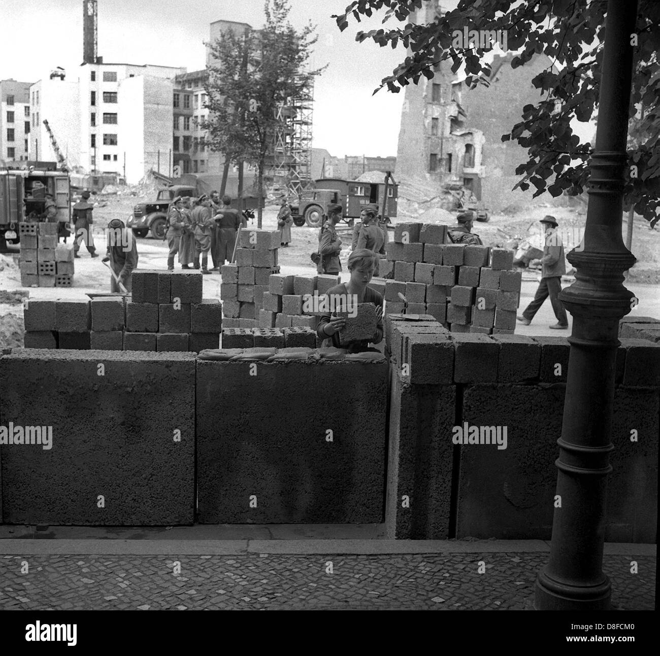 Les travailleurs de la construction de Berlin est d'étendre le Mur de Berlin à partir de la "Potsdamer Platz", dans le sens de 'Lindenstrasse' street sous la supervision d'agents armés de la police de Berlin, RDA, 18 août 1961. Le mur est construit entre deux et cinq mètres à l'intérieur de la ligne de démarcation des secteurs dans Berlin Est. Ici, les frontières des secteurs courent le long de la chambre les façades. Grit et dalles de béton, briques creuses qui ont été initialement conçus pour la construction de maisons à Berlin Est, sont utilisés pour la construction. Les travailleurs de la construction sont payés 1,28 marks d'une heure. Dans Banque D'Images