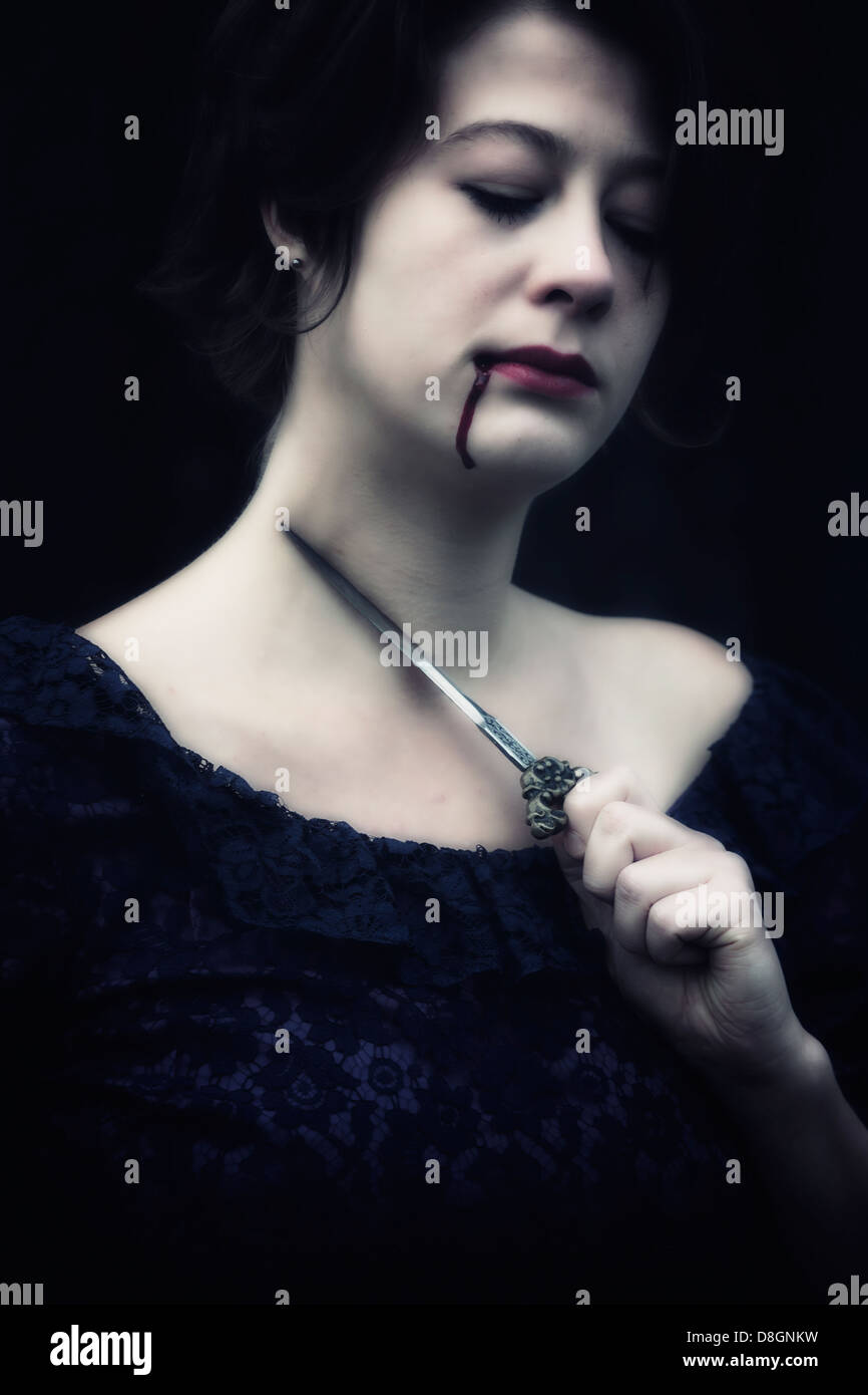 Une femme dans une robe sombre tient un poignard à la gorge, avoir de sang dégoulinant de sa bouche Banque D'Images
