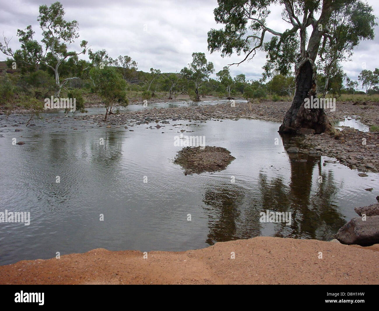 Une oasis sereine dans le désert avec un petit plan d'eau entouré de palmiers et d'un paysage désertique aride. Le papier peint met en valeur le contraste frappant entre l'environnement sec et l'eau rafraîchissante. Banque D'Images