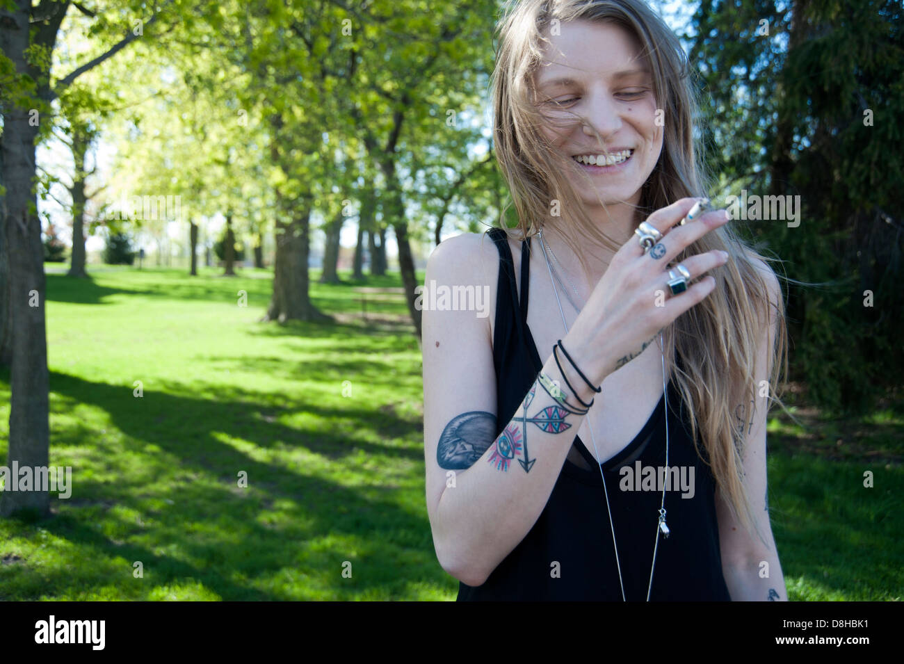 Jolie jeune femme moderne dans un parc de rire et de fumer une cigarette, les tatouages sur ses bras, Banque D'Images