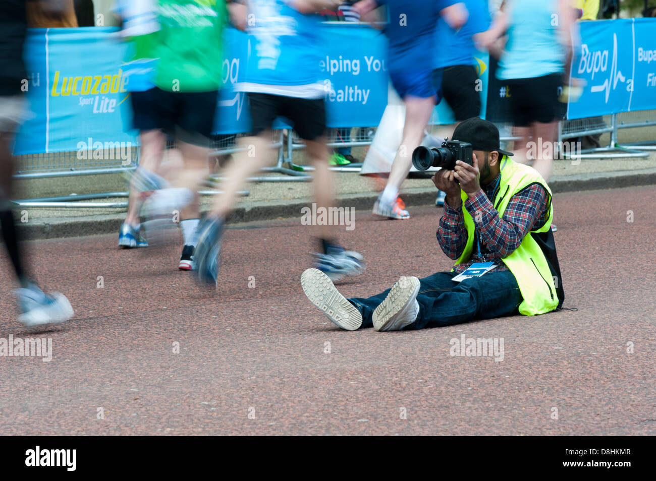 Un marathon photo photographe prenez des photos sur la course 10k BUPA Londres 2013, assis sur route avec lui coureurs se trouble Banque D'Images