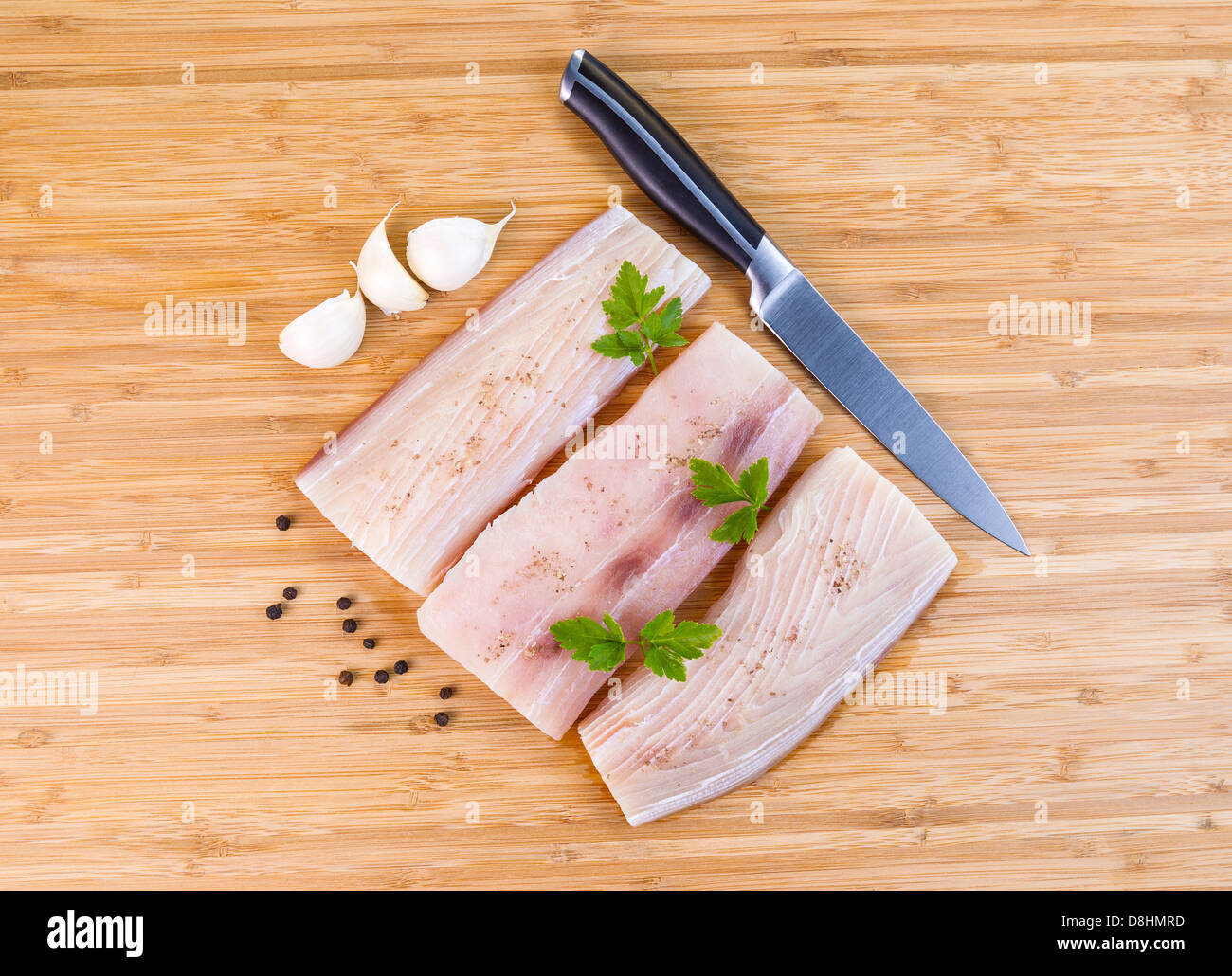 Photo horizontale de filets de poisson blanc, couteau, persil, ail et poivre de voirie sur fond de bois de bambou naturel Banque D'Images