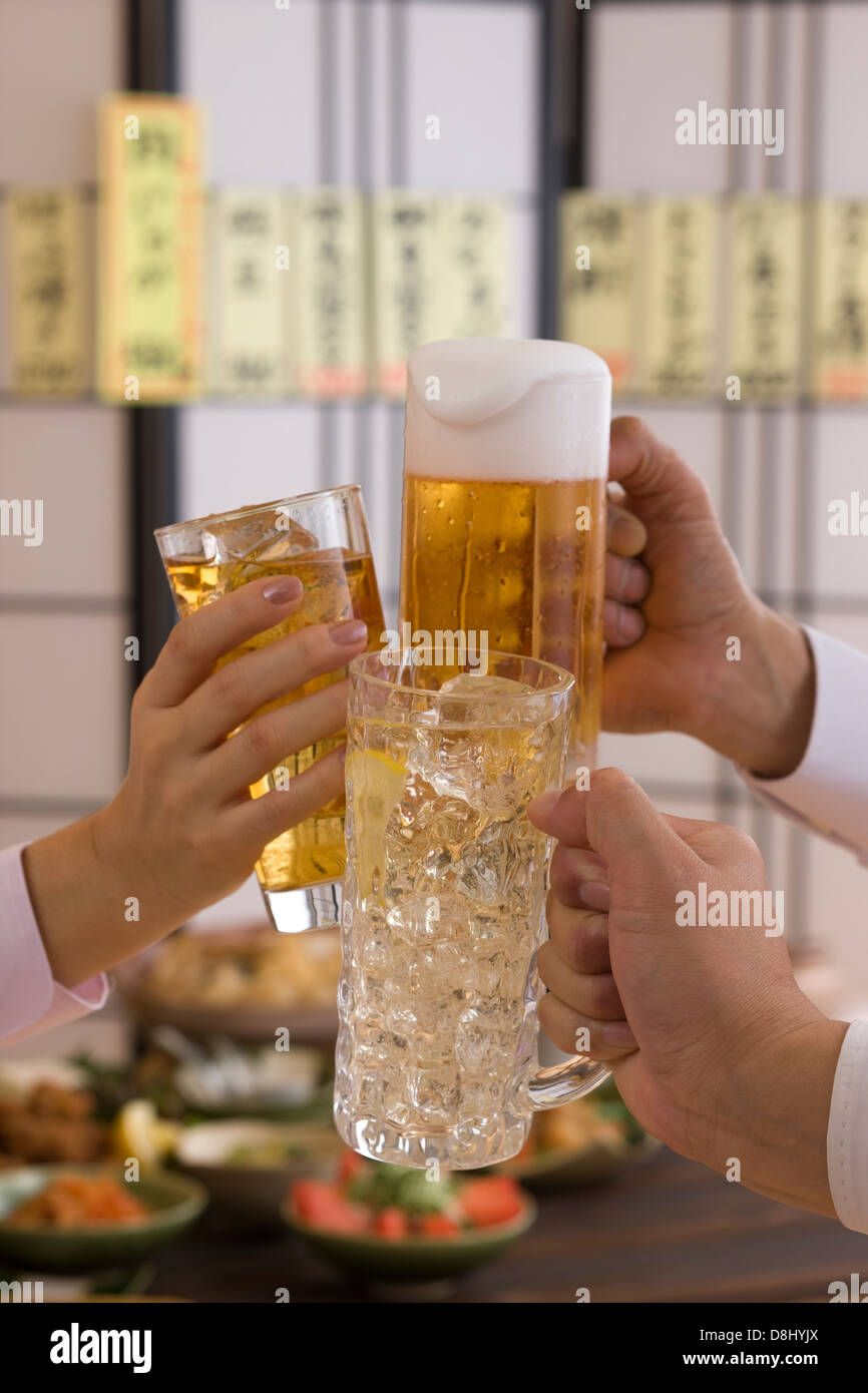 Trois personnes Toasting les uns avec les autres avec des boissons diverses à l'izakaya Banque D'Images