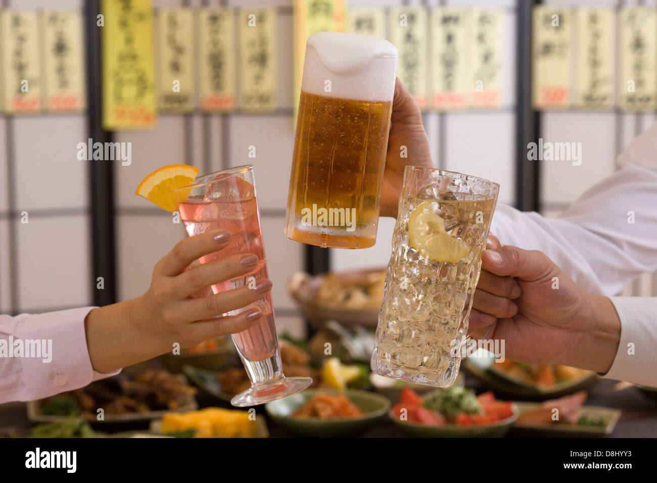 Trois personnes Toasting les uns avec les autres avec des boissons diverses à l'izakaya Banque D'Images