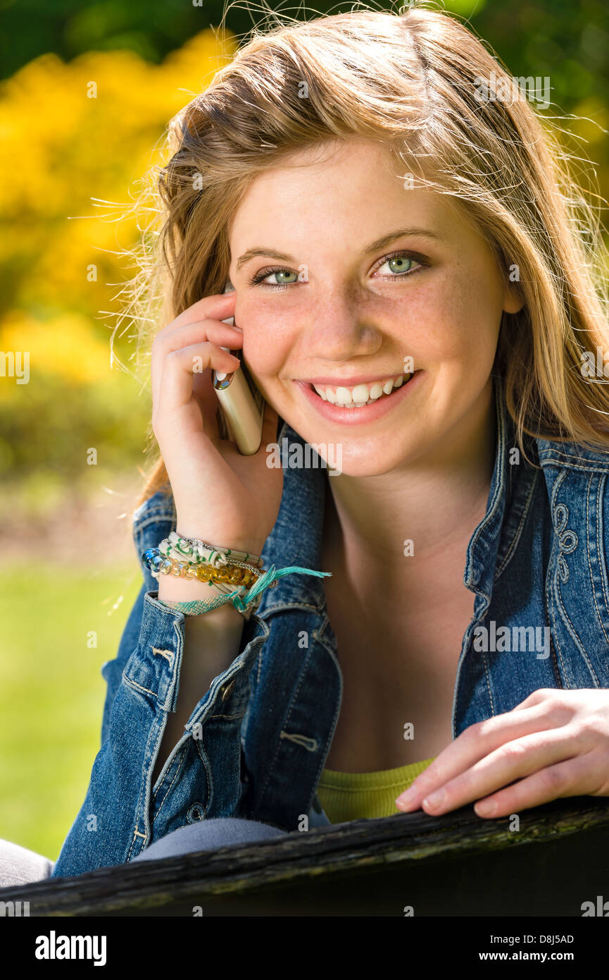 Adolescente joyeuse en utilisant son téléphone portable dans le parc Banque D'Images