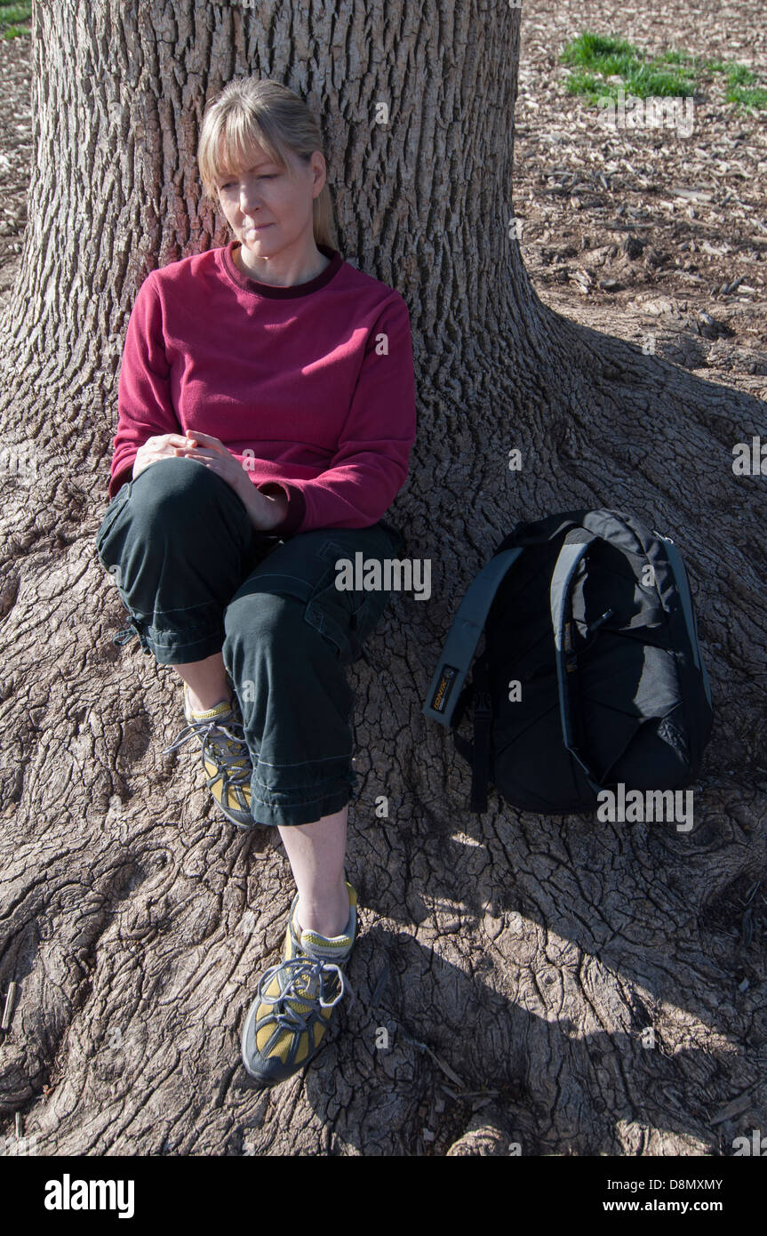 Femme avec expression de tristesse assis sous un arbre sur les racines. Banque D'Images