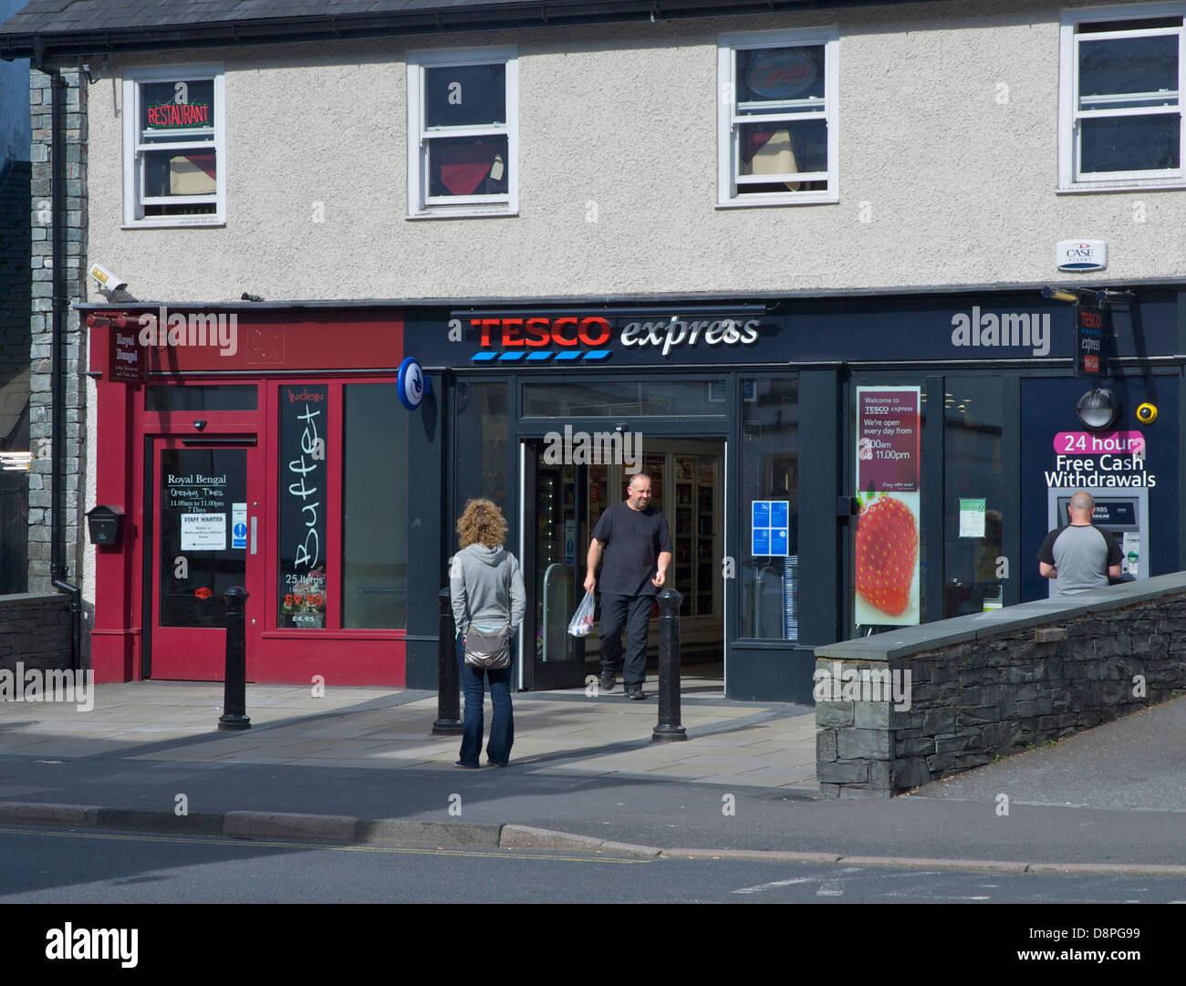 Homme marchant hors de la Tesco Express store à Ambleside, Parc National de Lake District, Cumbria, Angleterre, Royaume-Uni Banque D'Images