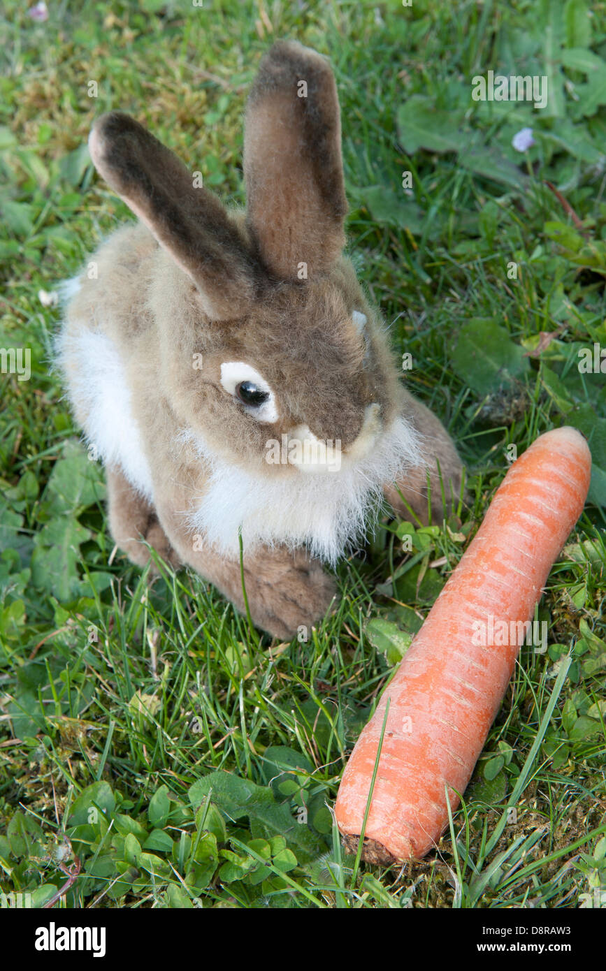 Lapin en peluche assis sur l'herbe à la carotte Banque D'Images