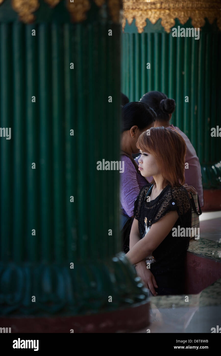Une jeune femme attend à l'ombre entre les colonnes vertes dans le complexe du temple Schwedagon à Rangoon (Yangon) Birmanie (Myanmar). Banque D'Images