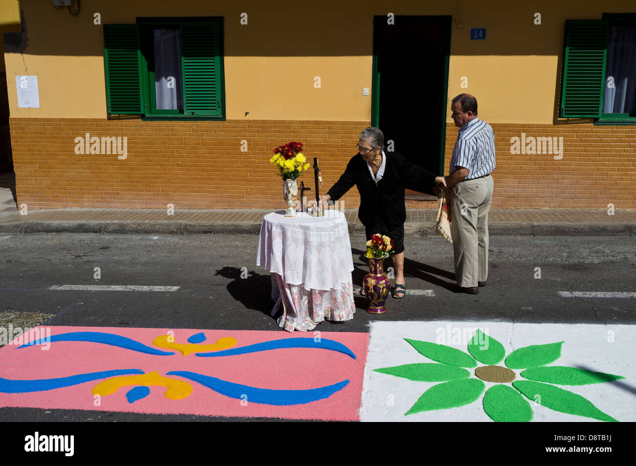 Corpus Christi de Alcala, vieille dame en noir met un crucifix sur un autel temporaire à l'extérieur de sa maison, s'accrochant à son fils pour Banque D'Images