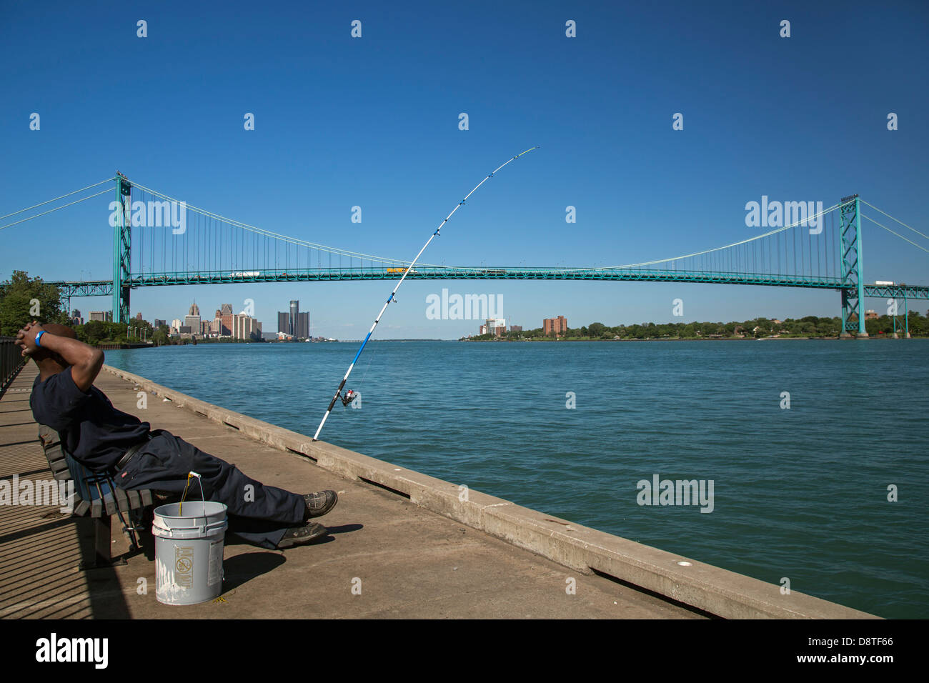 Un homme pêche de doré jaune dans la rivière Detroit en dessous du pont Ambassador. Banque D'Images