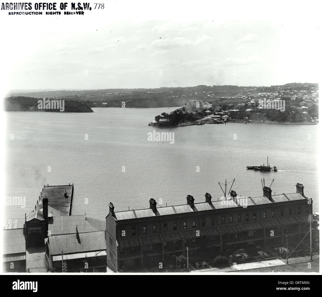 Cette photographie en noir et blanc capture une vue panoramique du port de Sydney, mettant en valeur le port emblématique et le paysage urbain environnant. Il offre une perspective historique sur le paysage de la Nouvelle-Galles du Sud. Banque D'Images