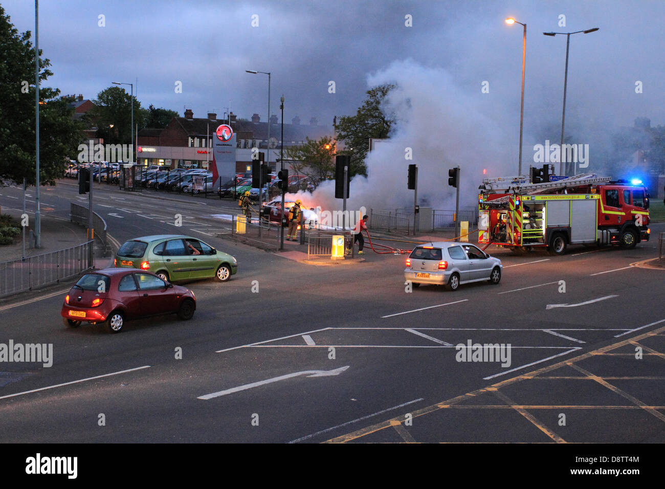 Voiture en feu accident au croisement, feu de circulation fumée, pompiers arrêter l'incendie, Norfolk, Royaume-Uni Banque D'Images
