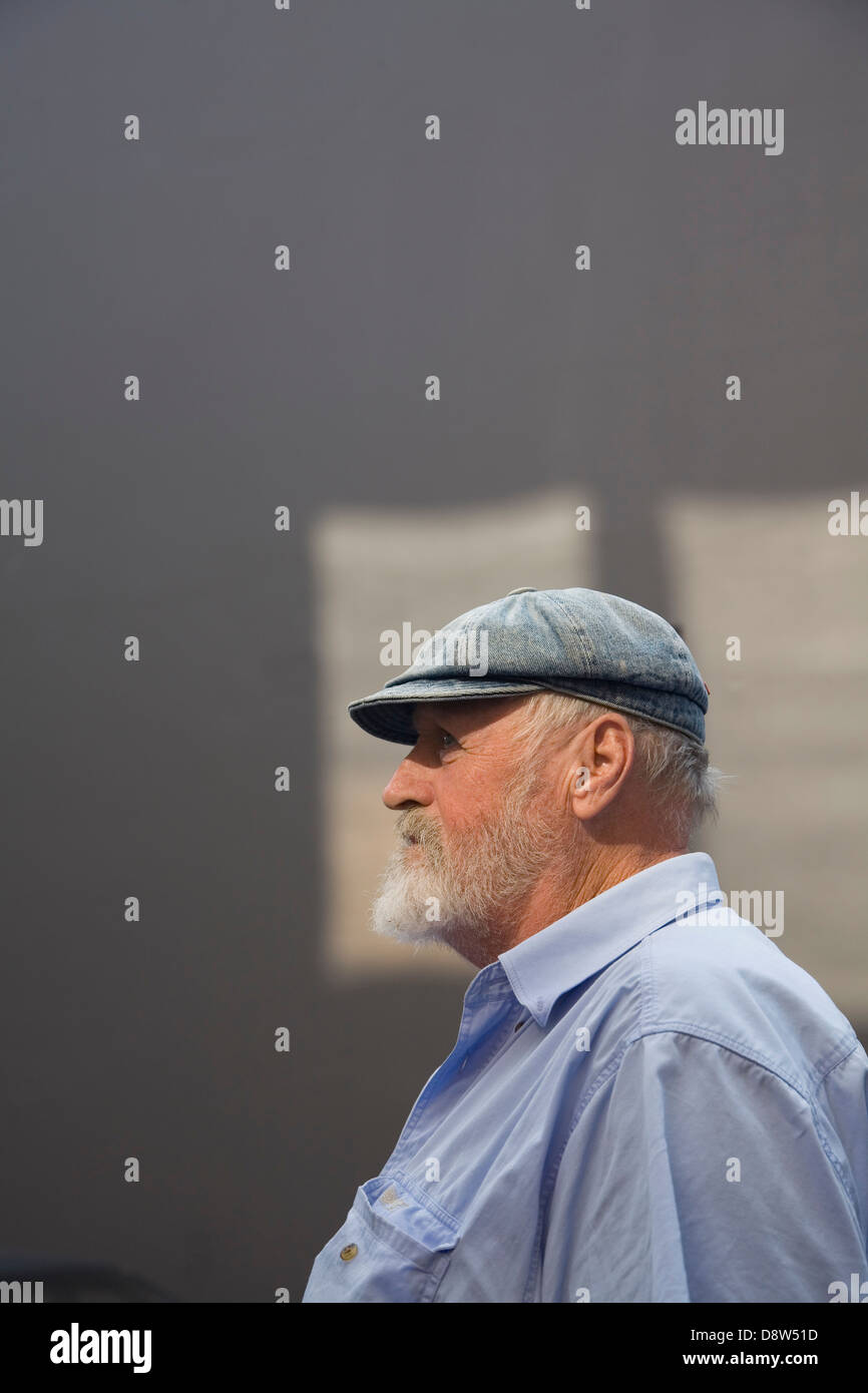 Homme de 50 ans, avec barbe grise, portant casquette et chemise bleue,  contre un mur gris avec des taches de soleil, de profil Photo Stock - Alamy