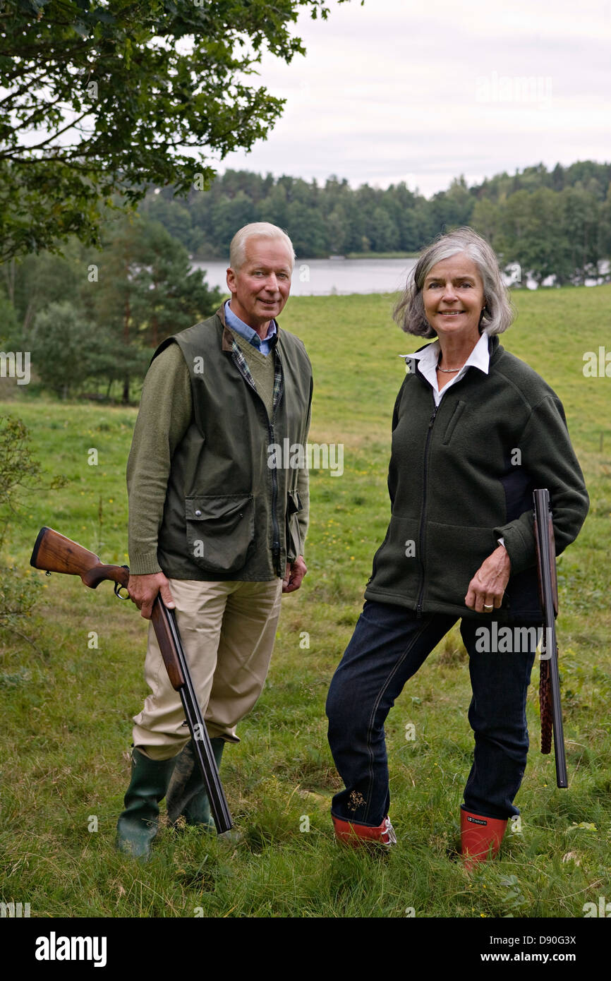 Senior couple holding rifle standing on grass, smiling Banque D'Images