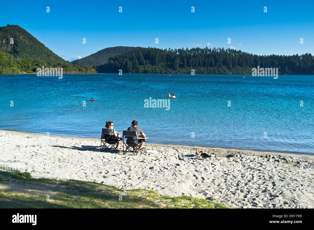dh Blue Lake ROTOROA NEW ZEALAND couple assis sur sable plage lac Tikitapu vacances Banque D'Images