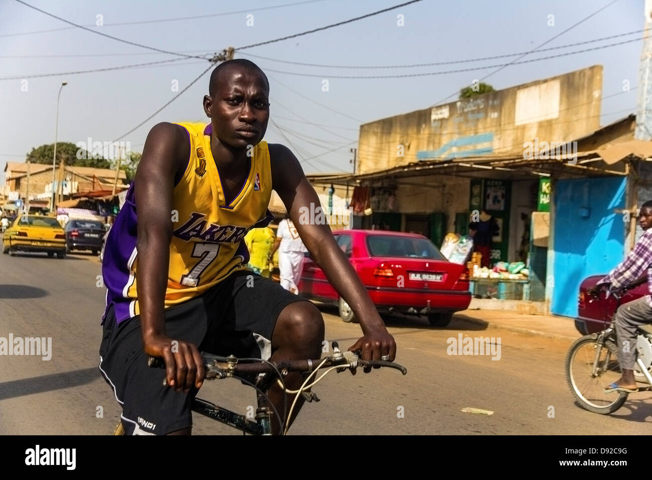 Cycliste avec t-shirt lakers dans une rue de Serrekunda, Gambie Banque D'Images