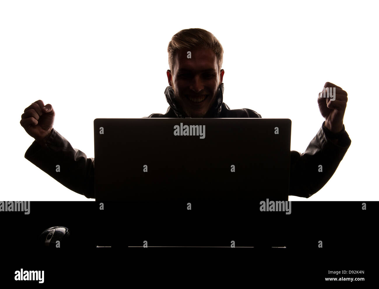 Beau modèle masculin derrière un ordinateur portable sur son bureau avec work et fond blanc, la création d'une silhouette, exprimant la joie. Banque D'Images